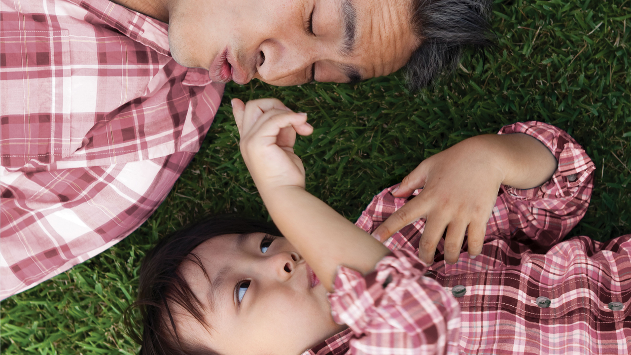 爸爸與兒子在草地上；圖片使用「於駿富保障萬用壽險計劃頁面」。