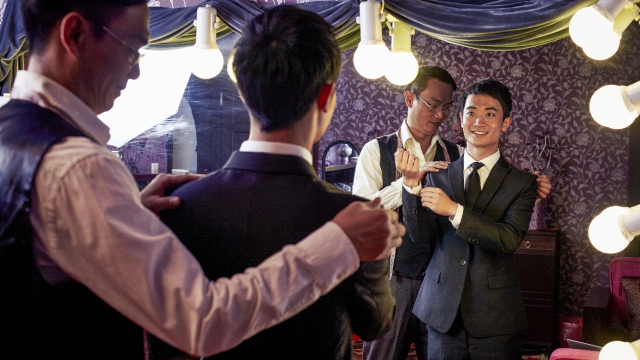 A tailor is taking body measurements for a young man; image used for Wealth products.