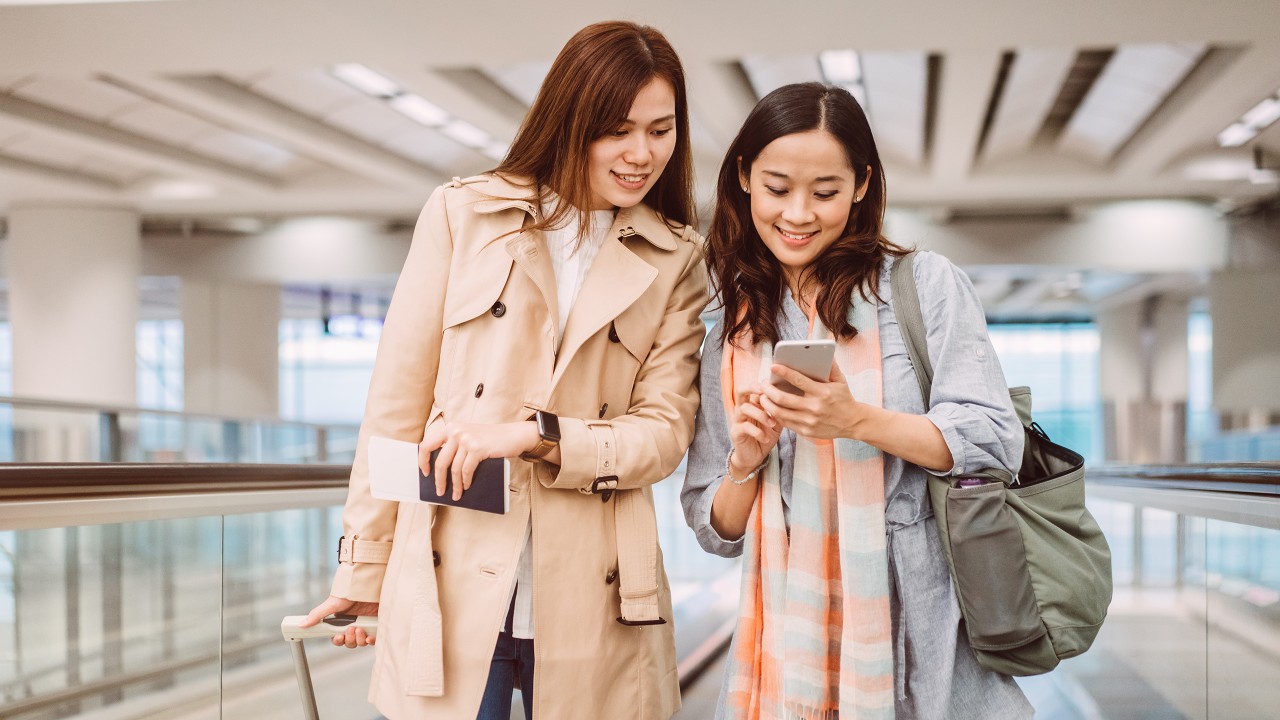 两位女士在机场使用手机；图片用于汇丰24小时外币兑换服务页面