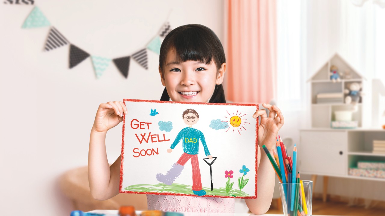 Daughter holding up a 'get well soon' card for her father