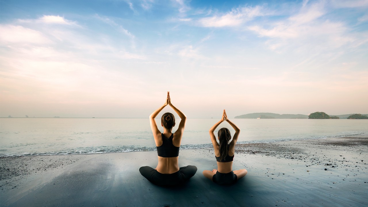 两个女人在海滩上做瑜伽，图像用于"暑假亲子游，让孩子学懂珍惜大自然"的文章