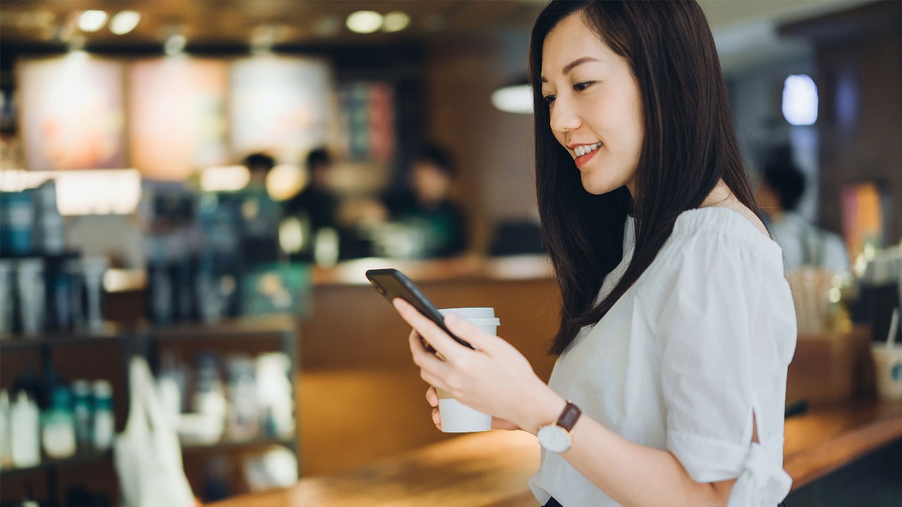 女人在咖啡店里看手机；圖像用於商戶免息分期付款計劃