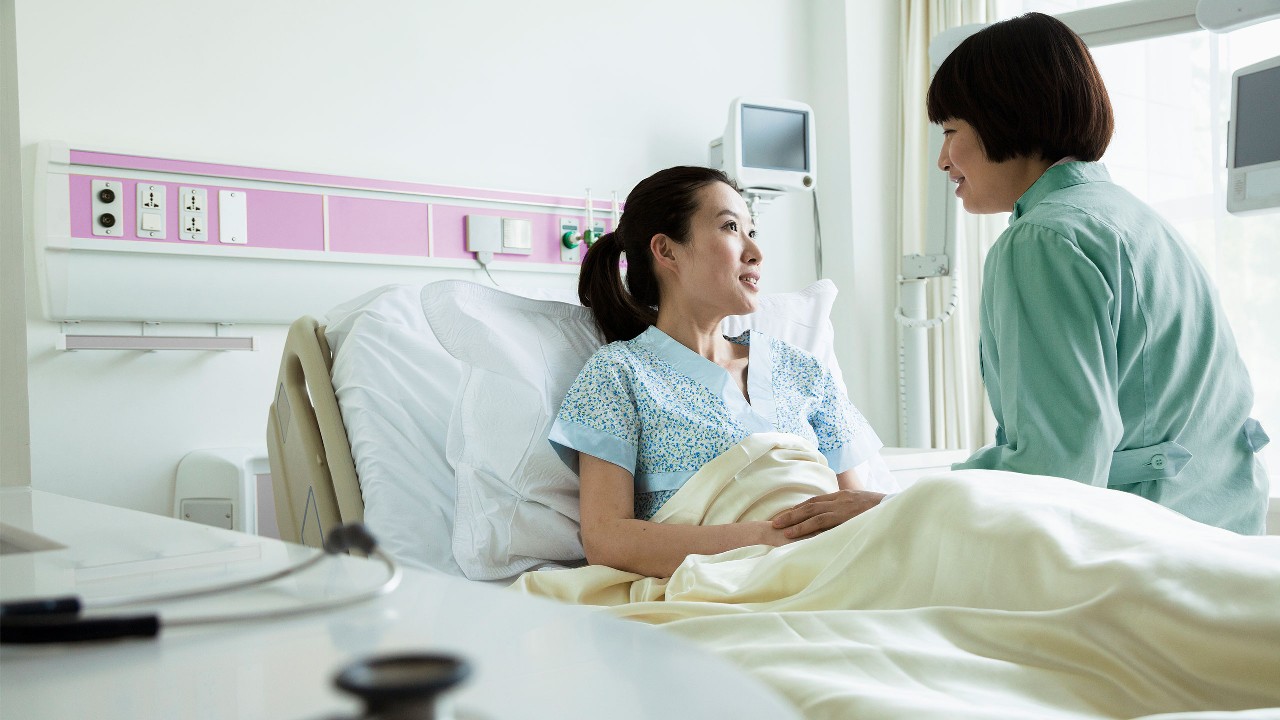 醫生坐在病床上與病人討論病情；圖片使用於危疾和癌症保障。
