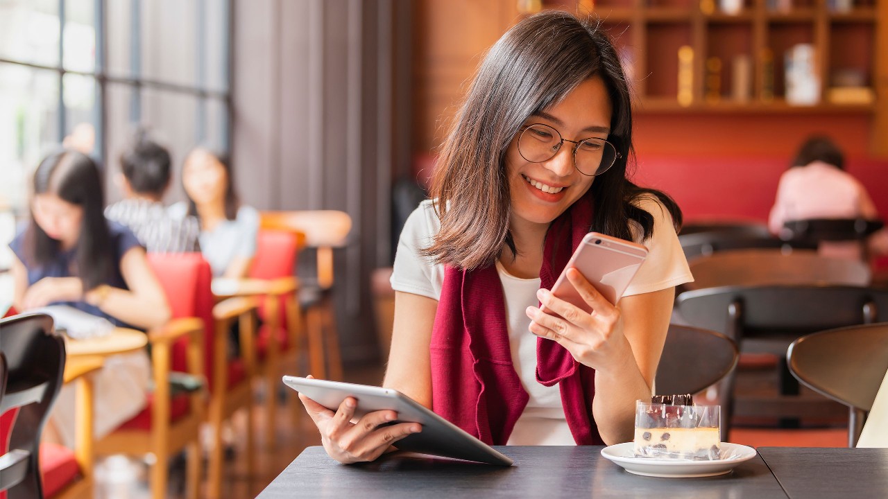 A smiling woman is looking at her phone while holding a tablet; image used for the HSBC Hong Kong Ways to Bank page.