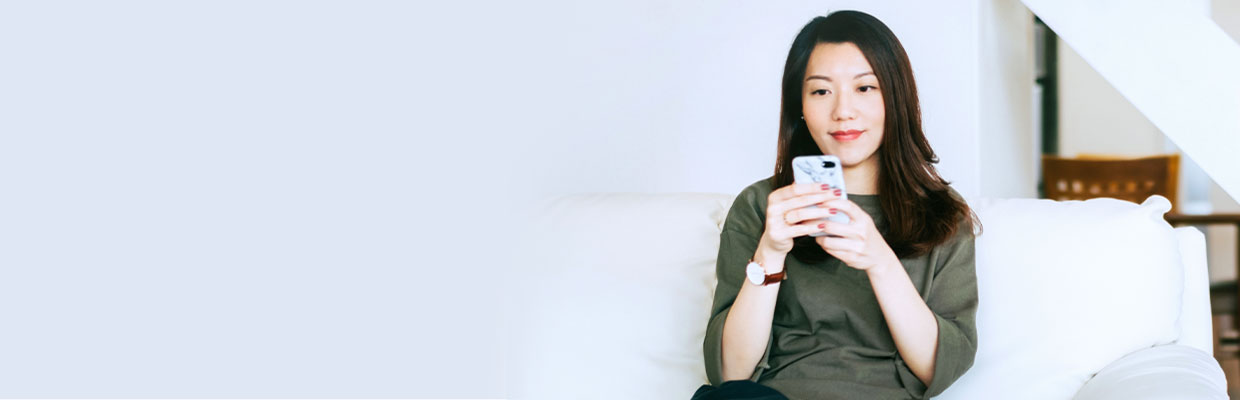 Woman is holding a smartphone on the sofa; image used for "Home loving" article.