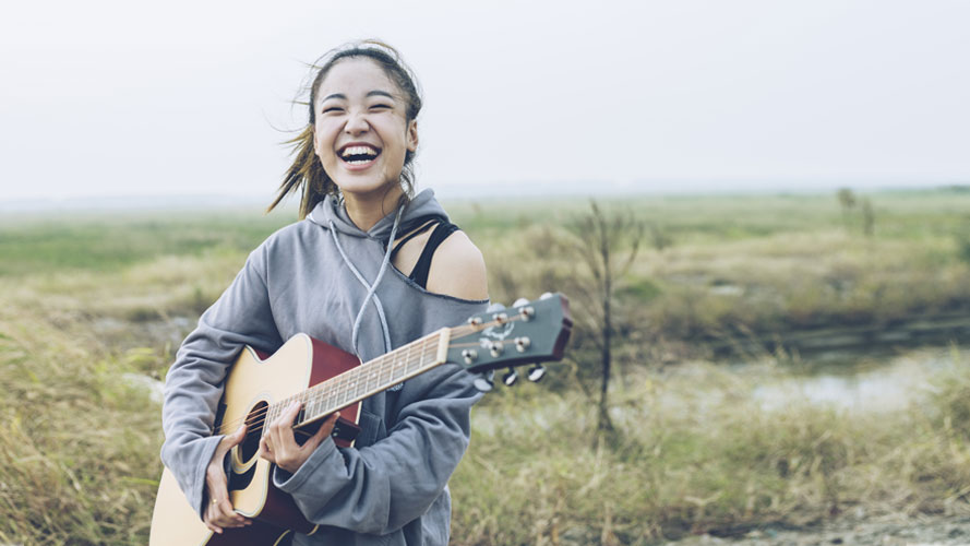 Fashionable girl playing guitar on country road; the image used for "5 steps to grow your savings" article.