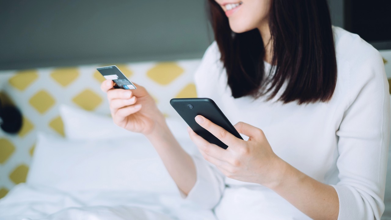 Smiling woman is holding a mobile phone and a bank ATM card; image used for the HSBC Hong Kong WeChat page.